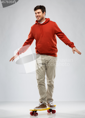 Image of smiling young man in hoodie riding on skateboard