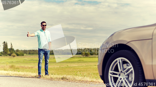 Image of man hitchhiking and stopping car at countryside