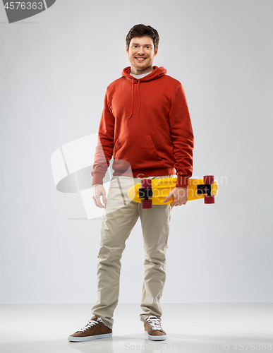 Image of smiling young man in hoodie with short skateboard