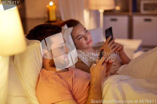 Image of couple using smartphones in bed at night