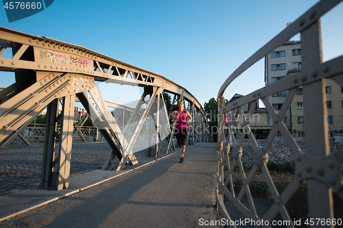 Image of woman jogging across the bridge at sunny morning