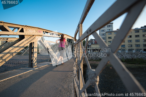 Image of woman jogging across the bridge at sunny morning