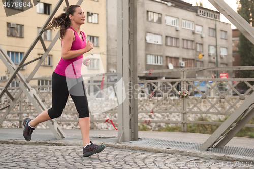 Image of woman jogging across the bridge at sunny morning