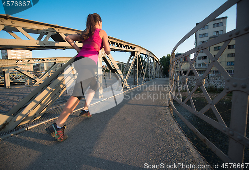 Image of woman jogging across the bridge at sunny morning