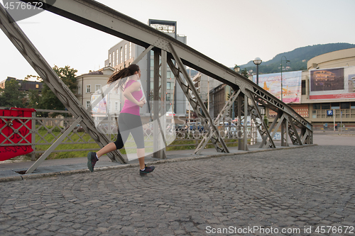 Image of woman jogging across the bridge at sunny morning