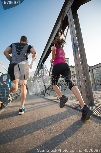 Image of young couple jogging across the bridge in the city