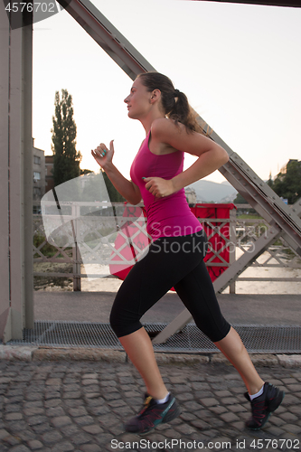 Image of woman jogging across the bridge at sunny morning