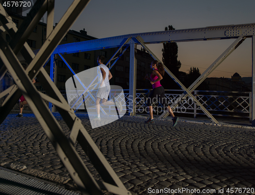 Image of portrait of couple jogging across the bridge in the city