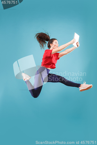 Image of Image of young woman over pink background using laptop computer or tablet gadget while jumping.