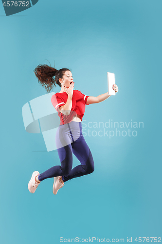 Image of Image of young woman over pink background using laptop computer or tablet gadget while jumping.