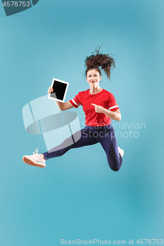 Image of Image of young woman over pink background using laptop computer or tablet gadget while jumping.