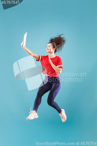 Image of Image of young woman over pink background using laptop computer or tablet gadget while jumping.