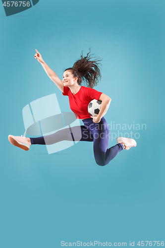 Image of Forward to the victory.The young woman as soccer football player jumping and kicking the ball at studio on pink