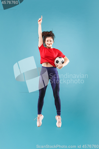 Image of Forward to the victory.The young woman as soccer football player jumping and kicking the ball at studio on pink