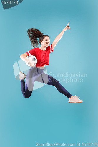 Image of Forward to the victory.The young woman as soccer football player jumping and kicking the ball at studio on pink