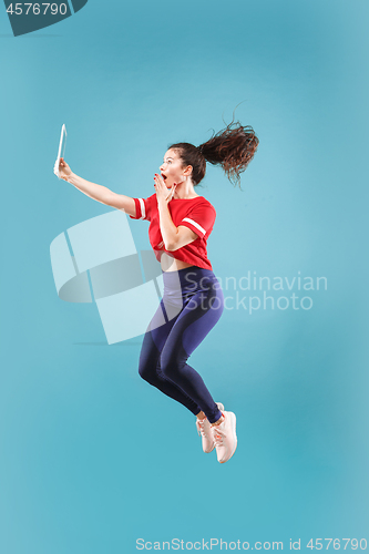 Image of Image of young woman over pink background using laptop computer or tablet gadget while jumping.