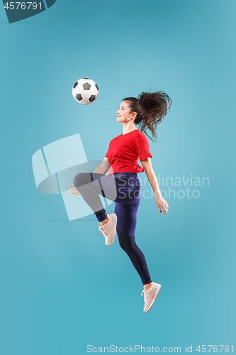 Image of Forward to the victory.The young woman as soccer football player jumping and kicking the ball at studio on pink