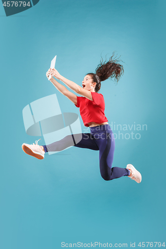 Image of Image of young woman over pink background using laptop computer or tablet gadget while jumping.