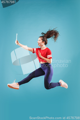 Image of Image of young woman over pink background using laptop computer or tablet gadget while jumping.