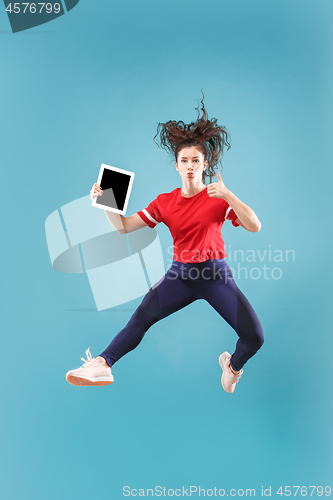 Image of Image of young woman over pink background using laptop computer or tablet gadget while jumping.