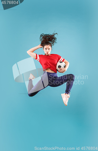 Image of Forward to the victory.The young woman as soccer football player jumping and kicking the ball at studio on pink