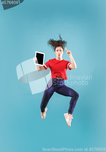 Image of Image of young woman over pink background using laptop computer or tablet gadget while jumping.