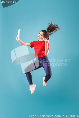 Image of Image of young woman over pink background using laptop computer or tablet gadget while jumping.