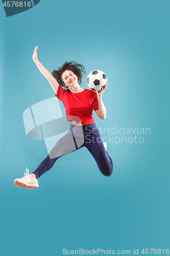 Image of Forward to the victory.The young woman as soccer football player jumping and kicking the ball at studio on pink