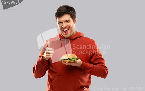 Image of happy young man with hamburger showing thumbs up