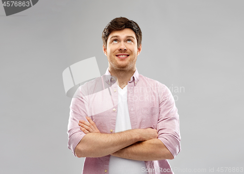 Image of smiling young man with crossed hands looking up