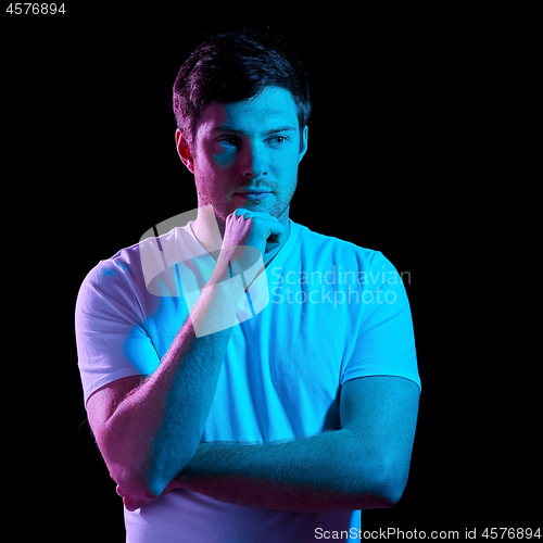 Image of thinking man over neon lights in dark room