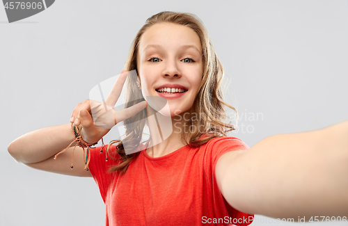 Image of smiling woman taking selfie and showing peace sign