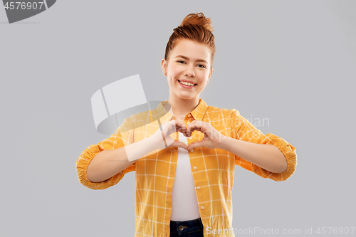 Image of smiling red haired teenage girl making hand heart