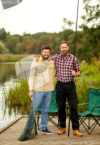 Image of friends with fishing rods and net at lake or river