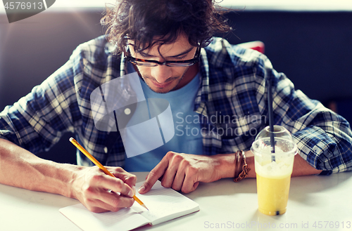 Image of man with notebook and juice writing at cafe