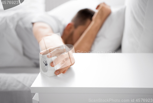 Image of close up of man in bed reaching for alarm clock