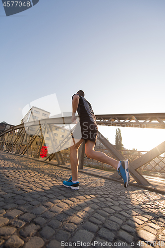 Image of man jogging across the bridge at sunny morning