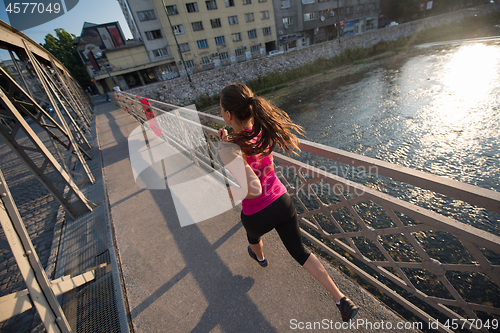 Image of woman jogging across the bridge at sunny morning