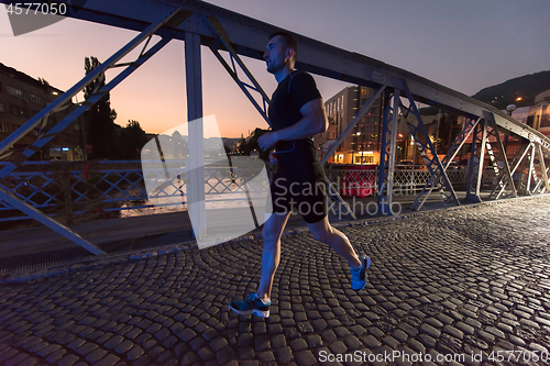 Image of man jogging across the bridge in the city