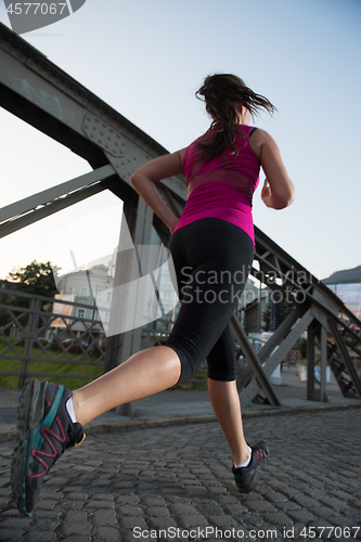 Image of woman jogging across the bridge at sunny morning