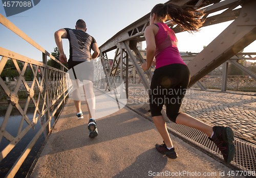 Image of young couple jogging across the bridge in the city