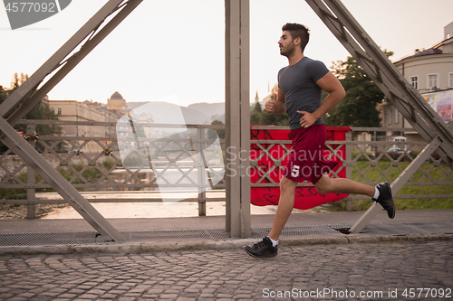 Image of man jogging across the bridge at sunny morning