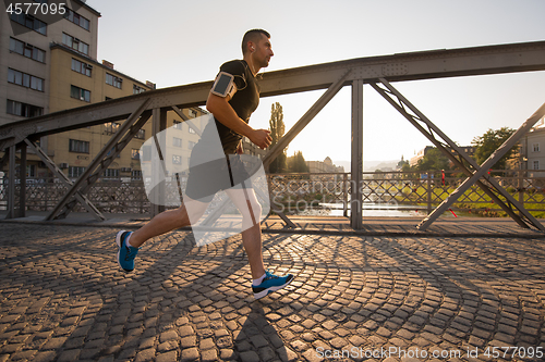 Image of man jogging across the bridge at sunny morning