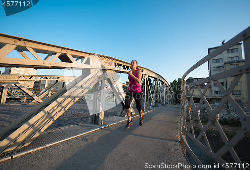 Image of woman jogging across the bridge at sunny morning