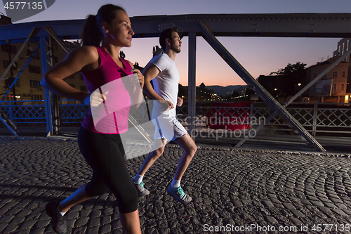 Image of couple jogging across the bridge in the city