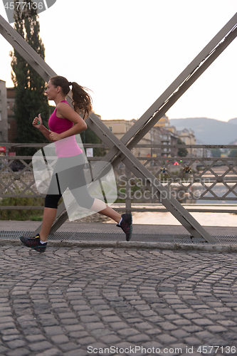 Image of woman jogging across the bridge at sunny morning