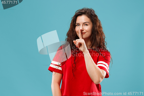 Image of The young woman whispering a secret behind her hand over blue background