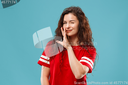 Image of The young woman whispering a secret behind her hand over blue background