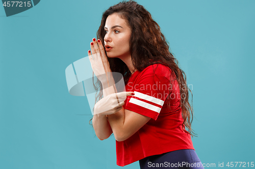 Image of The young woman whispering a secret behind her hand over blue background