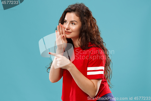 Image of The young woman whispering a secret behind her hand over blue background